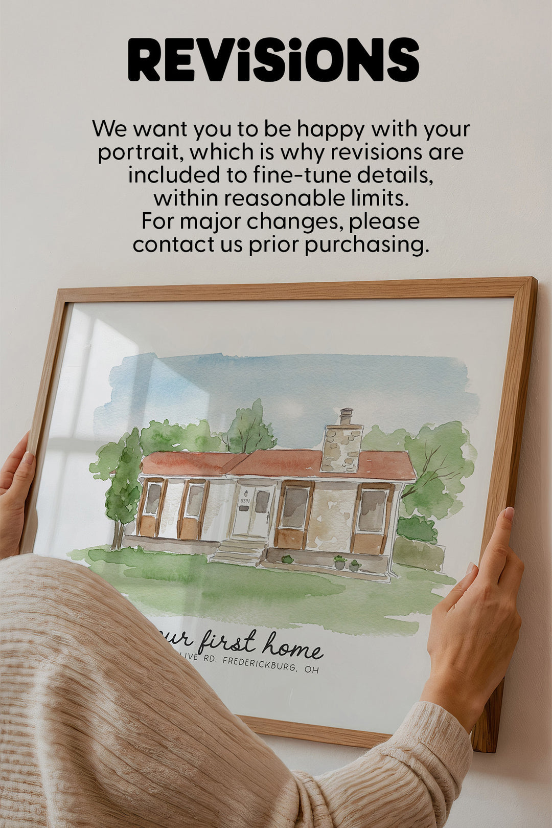 A framed watercolor portrait print of a house with the text 'REVISIONS' above it, held by hands wearing a beige sweater. The print includes a light wood frame and a white mat with a watercolor illustration of a home in soft green, brown, and blue tones.